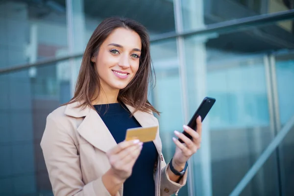Low Angle Of Pleased Girl Standing at the Airport Hall. He is Using Gold Credit card and Cellphone For Paying — Stock Photo, Image