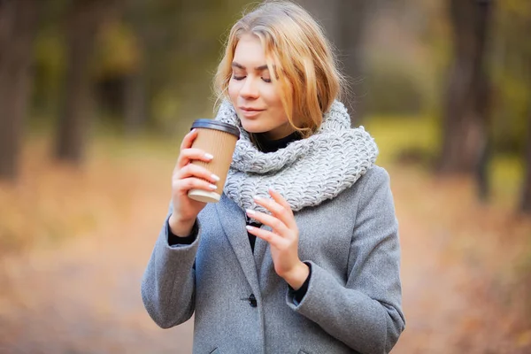 Coffee to go. Young woman with coffee in the autumn park