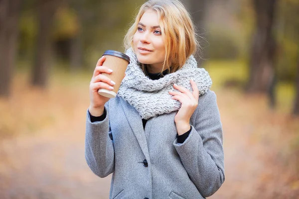 Coffee to go. Young woman with coffee in the autumn park