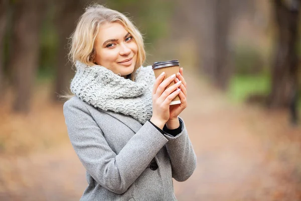 Coffee to go. Young woman with coffee in the autumn park