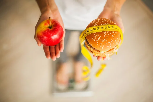 Diet. Woman Measuring Body Weight On Weighing Scale Holding Burger and red apple. Sweets Are Unhealthy Junk Food. Weight Loss. Obesity. Top View