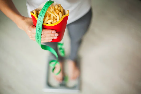 Kost. Kvinna mäta kroppsvikt på våg som håller ohälsosamma skräpmat. Viktminskning. Fetma. Ovanifrån — Stockfoto