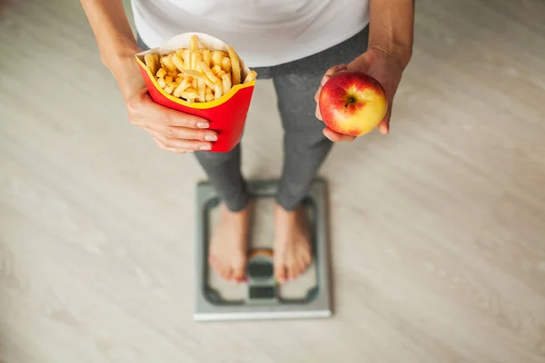 Dieta. Mulher medindo o peso corporal na balança segurando alimentos insalubres. Perda de peso. Obesidade. Vista superior — Fotografia de Stock