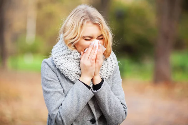 Una joven sonándose la nariz en el parque. Mujer retrato al aire libre estornudos porque el frío y la gripe — Foto de Stock