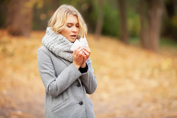 Young woman blowing her nose on the park. Woman portrait outdoor sneezing because cold and flu — Stock Photo, Image