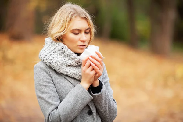 Una joven sonándose la nariz en el parque. Mujer retrato al aire libre estornudos porque el frío y la gripe — Foto de Stock