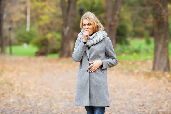 Erkältung und Grippe. junge Frau im grauen Mantel spaziert durch den Herbstpark und wärmt gefrorene Hand — Stockfoto