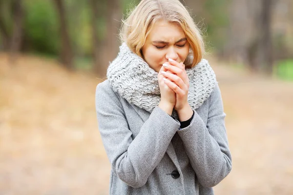 Dingin dan flu. Wanita muda dalam mantel abu-abu berjalan di taman musim gugur dan menghangatkan tangan beku — Stok Foto