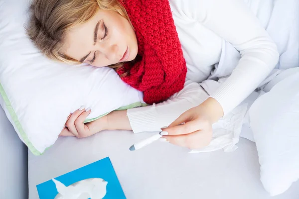 Frío y gripe. Mujer enferma acostada en una cama con un termómetro — Foto de Stock