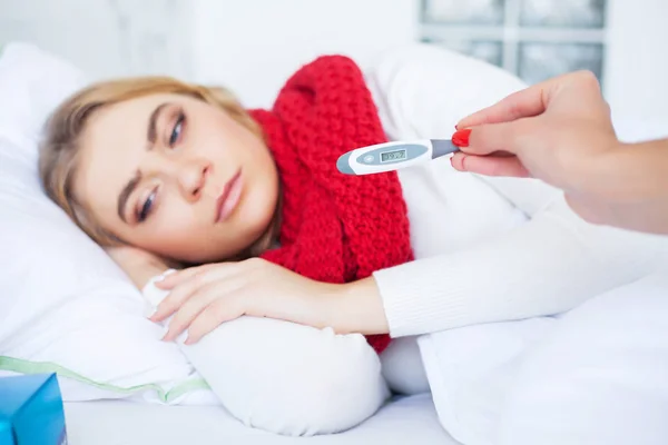 Zima a chřipky. Nemocná žena leží na posteli s teploměrem — Stock fotografie