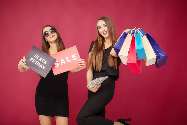 Vásárlás. Két nő gazdaság színes táska piros háttéren fekete péntek nyaralás — Stock Fotó