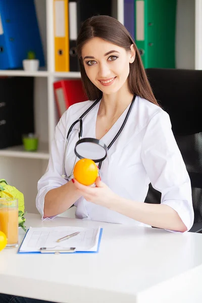 Salud. Doctor Dietologist Holds in the Fresh Orange Hands. Nutrición saludable. Verduras frescas y frutas sobre la mesa. Feliz Doctor en la Sala de Luz. Alta resolución —  Fotos de Stock