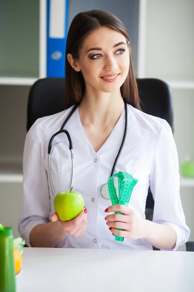 Salud. Retrato del afortunado dietista en la sala de luz. Sostiene la Manzana Verde y la Cinta del Centímetro. Nutrición saludable. Verduras y frutas frescas sobre la mesa —  Fotos de Stock