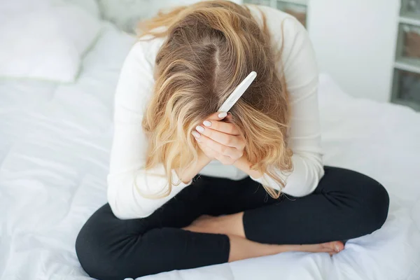 Prueba de embarazo positiva. Mujer joven sintiéndose deprimida y triste después de ver el resultado de la prueba de embarazo en casa — Foto de Stock