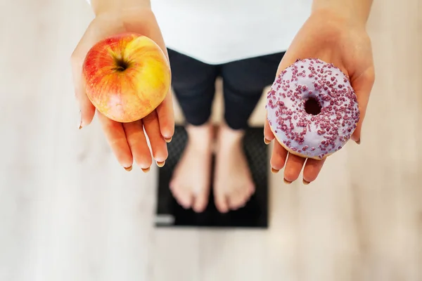 Diet. Woman Measuring Body Weight On Weighing Scale Holding Donut and apple. Sweets Are Unhealthy Junk Food. Fast Food