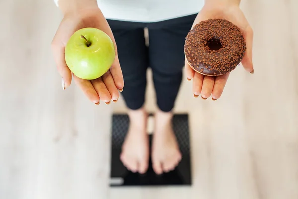 Dieet. Vrouw meten Body gewicht op wegen schaal Holding Donut en apple. Snoepjes zijn ongezonde junkfood. Fastfood — Stockfoto