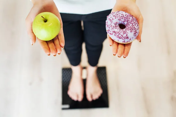 Dieet. Vrouw meten Body gewicht op wegen schaal Holding Donut en apple. Snoepjes zijn ongezonde junkfood. Fastfood — Stockfoto