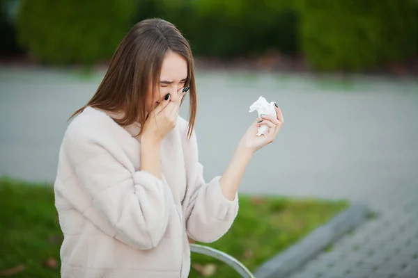 Resfriado y gripe. Joven chica atractiva, cogió un resfriado en la calle, se limpia la nariz con una servilleta — Foto de Stock