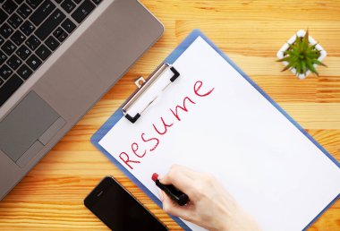 İş arama. Beyaz kağıt üzerine ruj ile el yazma devam. Ahşap ofis büro dizüstü bilgisayar, akıllı telefon ve malzemeleri