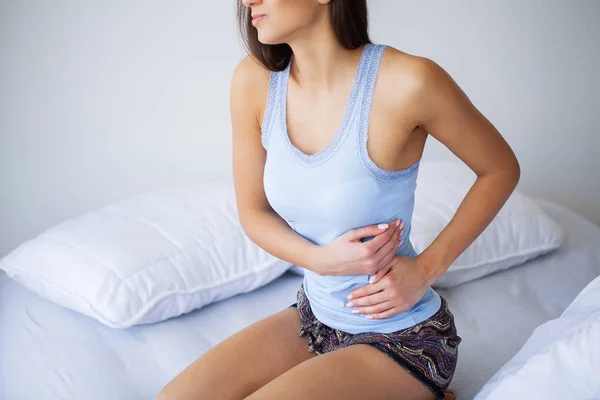 Dolor de estómago. Mujer joven malsana con dolor de estómago apoyada en la cama en casa — Foto de Stock