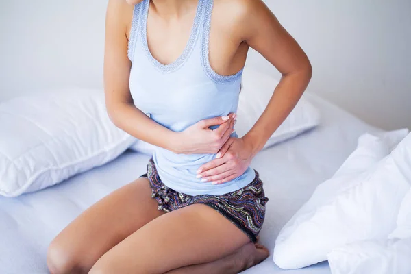 Dolor de estómago. Mujer joven malsana con dolor de estómago apoyada en la cama en casa — Foto de Stock