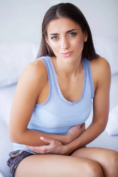 Dolor de estómago. Mujer joven malsana con dolor de estómago apoyada en la cama en casa — Foto de Stock