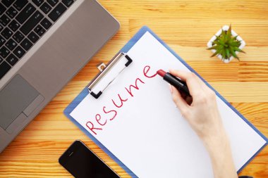 İş arama. Beyaz kağıt üzerine ruj ile el yazma devam. Ahşap ofis büro dizüstü bilgisayar, akıllı telefon ve malzemeleri