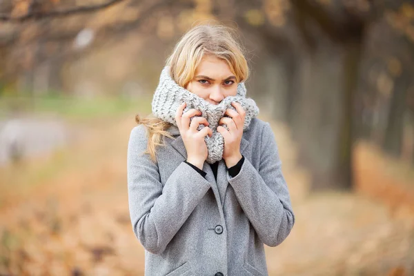 感冒和流感。穿着灰色外套走在秋园的年轻女子, 温暖冻僵的手 — 图库照片