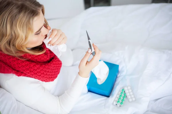 Kranke Frau. Frau mit Grippevirus liegt im Bett und misst ihre Temperatur mit Thermometer — Stockfoto