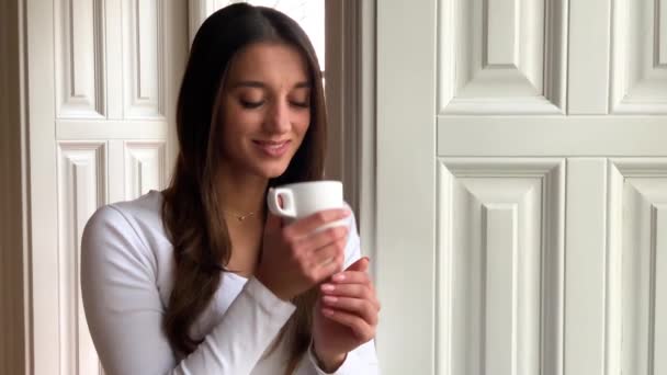 Красивая молодая девушка пьет кофе и улыбается в кафе — стоковое видео