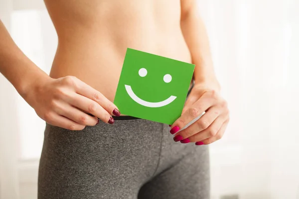 Women Health. Closeup Of Healthy Female With Beautiful Fit Slim Body In White Panties Holding White Card With Happy Smiley Face In Hands. Stomach Health And Good Digestion Concepts. High Resolution