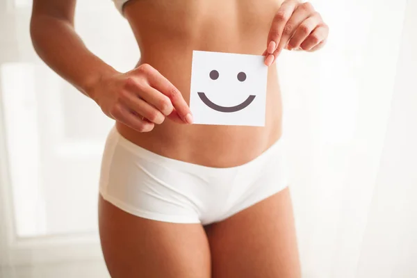 Salud de las mujeres. primer plano de la hembra sana con hermoso ajuste delgado cuerpo en bragas blancas sosteniendo tarjeta blanca con la cara sonriente feliz en las manos. Salud estomacal y buenos conceptos de digestión. Alta resolución — Foto de Stock