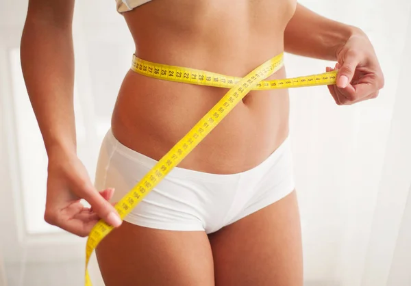 Mujer joven delgada midiendo su cintura delgada con una cinta métrica — Foto de Stock
