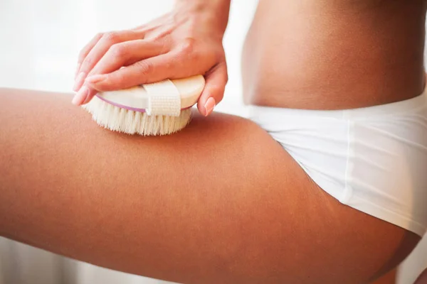 Womans arm holding dry brush to top of her leg. Cellulite treatment, dry brushing