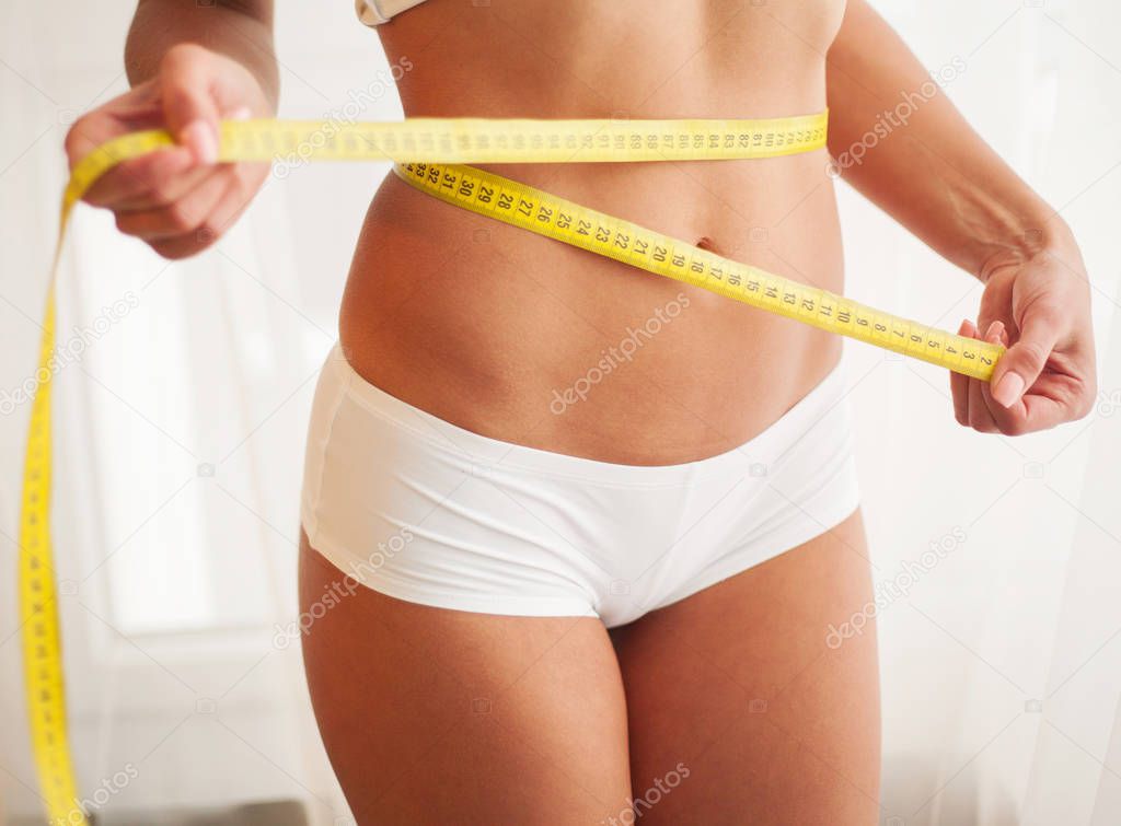 Slim young woman measuring her thin waist with a tape measure