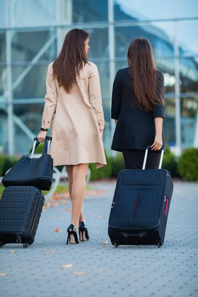 Zwei glückliche Mädchen, die zusammen ins Ausland reisen und Koffer im Flughafen tragen — Stockfoto