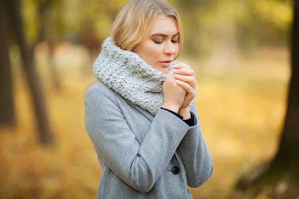 Cold and flu. Young woman in a gray coat walking in the autumn park and warms frozen hand — Stock Photo, Image