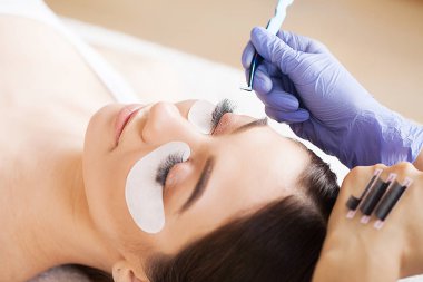 Kirpiklerini uzat. Sahte kirpikler. Kirpik uzatma prosedürü. Profesyonel stilist, kadın kirpiklerini uzatıyor. Usta ve bir müşteri güzellik salonunda.