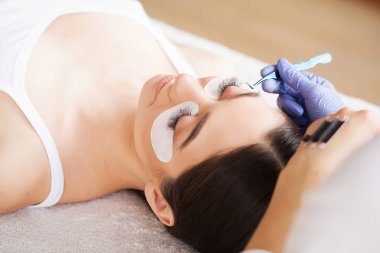 Kirpiklerini uzat. Sahte kirpikler. Kirpik uzatma prosedürü. Profesyonel stilist, kadın kirpiklerini uzatıyor. Usta ve bir müşteri güzellik salonunda.