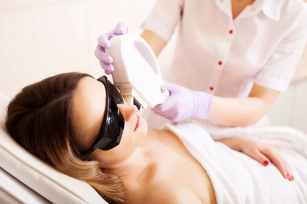 Pielęgnacja ciała. Zbliżenie kosmetyczki dając laserowe leczenie depilacji do młodej kobiety twarz — Zdjęcie stockowe