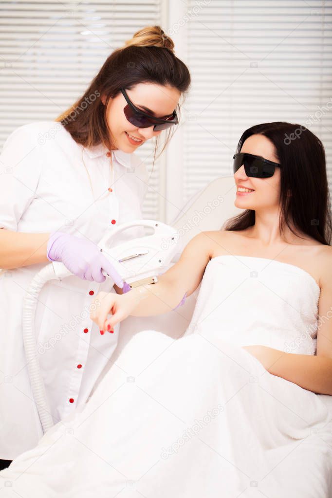 Body Care. Beautiful girl lies in the office of a beautician in goggles from laser irradiation, the hands of the doctor remove hair on hands with a laser device