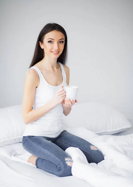 Ευτυχισμένη πρωί. Πορτρέτο του ένα χαμογελαστό γυναίκα όμορφη νεαρή μελαχρινή χαλάρωσης στο λευκό κρεβάτι — Φωτογραφία Αρχείου