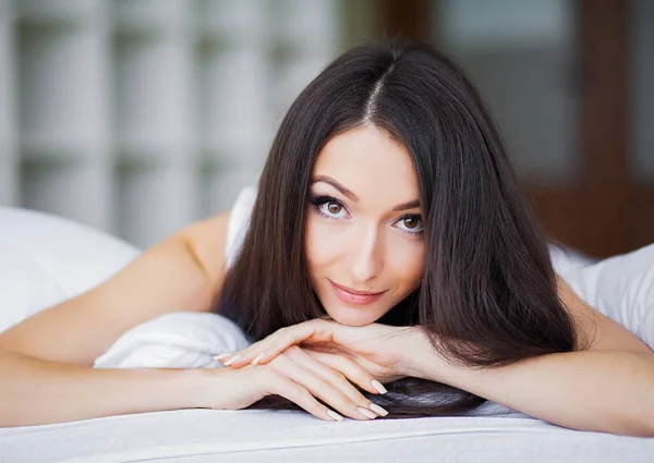 早晨快乐。一个微笑的漂亮年轻的黑发女人的肖像在白色的床上放松 — 图库照片