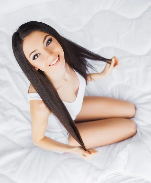 Szczęśliwy dzień. Portret uśmiechający się dość młoda brunetka kobieta relaksując się w łóżku biały — Zdjęcie stockowe
