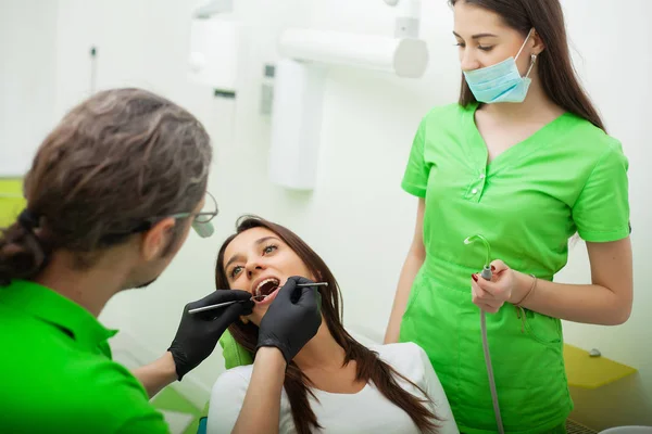 O dentista está a tratar dos dentes ao cliente no consultório dentário. — Fotografia de Stock