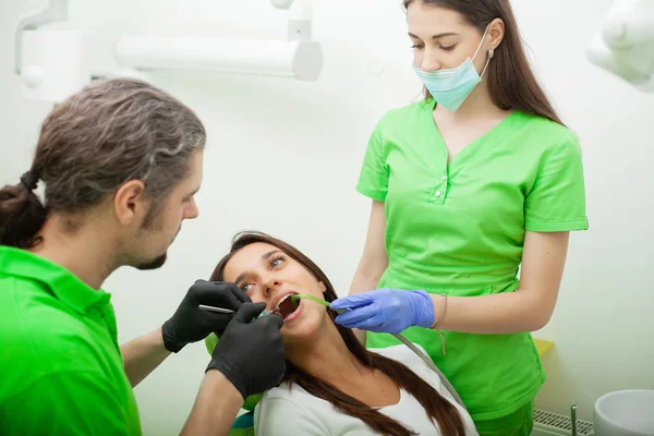 O dentista está a tratar dos dentes ao cliente no consultório dentário. — Fotografia de Stock