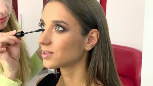 Salón de belleza. Joven modelo hermosa chica sentada en la silla. Maquillaje artista hace maquillaje niñas — Vídeo de stock