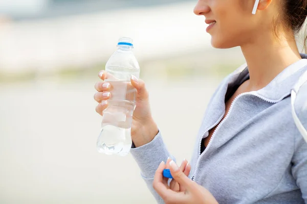 Fitness. Beautiful woman drinking water and listen to music after running