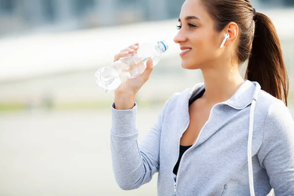 Фитнес. Красивая женщина пьет воду и слушает музыку после бега — стоковое фото
