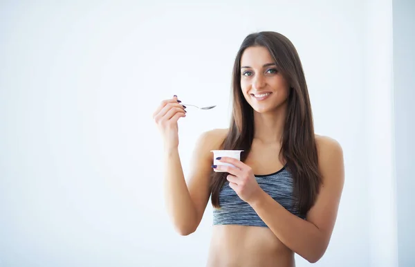 Diet. Happy young woman eating yogurt in kitchen